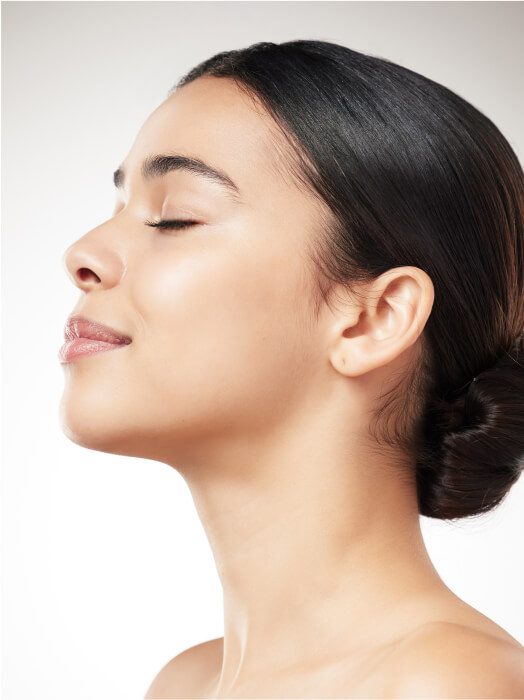 Profil d'une femme aux traits apaisés, peau lumineuse et bien-entretenue, cheveux noirs attachés