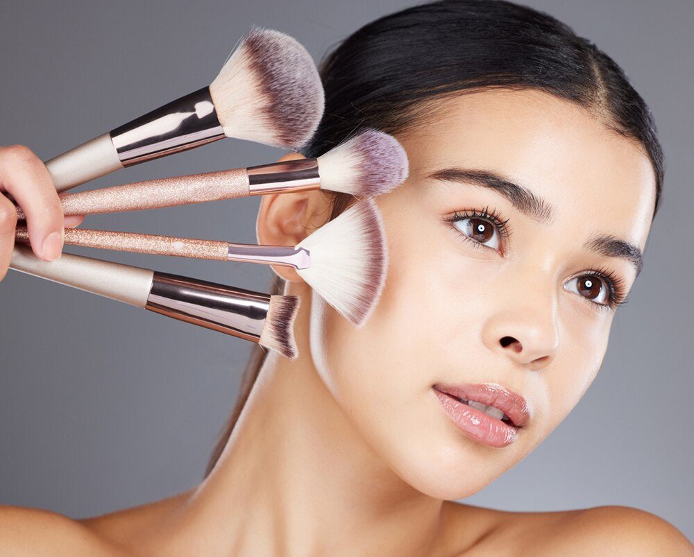 Femme appliquant des pinceaux de maquillage rose et noir sur son visage pour un maquillage professionnel