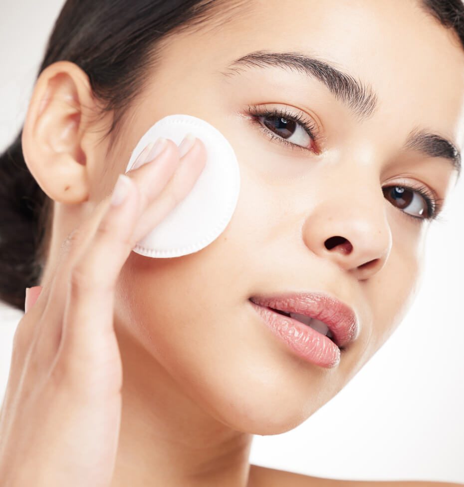Femme appliquant un disque démaquillant blanc sur son visage pour un soin de nettoyage cutané