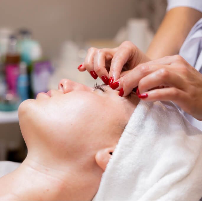 Esthéticienne appliquant des faux cils rouges sur les yeux d'une cliente en institut de beauté